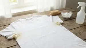 Maglietta bianca con macchie di sudore sotto le ascelle su un tavolo di legno accanto a spray e bicarbonato