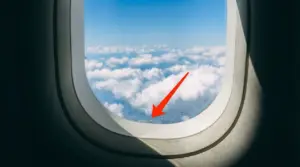 Finestrino di un aereo con vista sulle nuvole e un piccolo foro visibile in basso