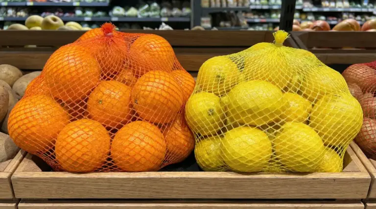Arance in rete arancione e limoni in rete gialla esposti su bancali di legno in un supermercato