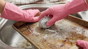 Mani con guanti rosa puliscono una teglia con sale grosso e una pallina di alluminio