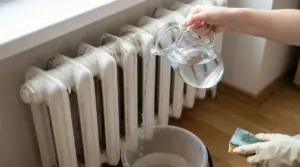 Persona versa acqua da una brocca su un termosifone sporco con un secchio sotto