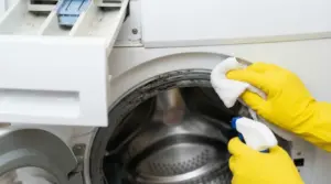 Persona con guanti pulisce la guarnizione della lavatrice con panno e spray